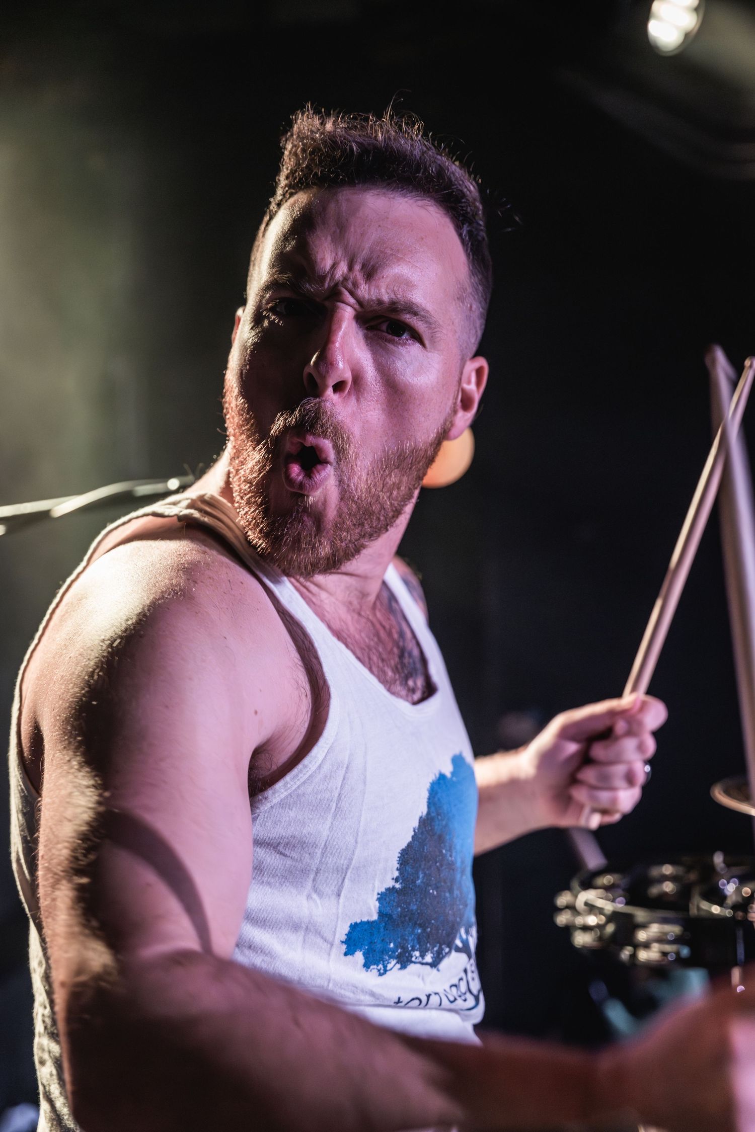 Passionate drummer performs intensely under dramatic stage lighting during a live show.