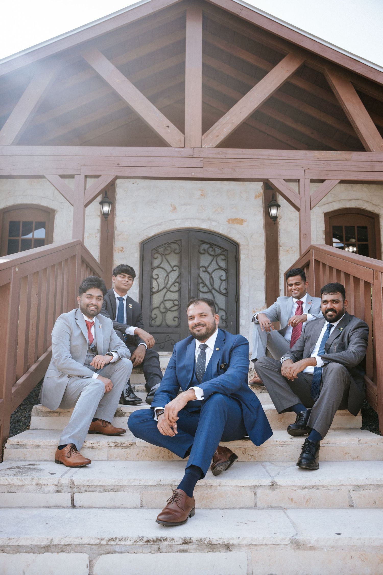 Wedding party relaxing on stone steps in coordinated grey and blue suits.