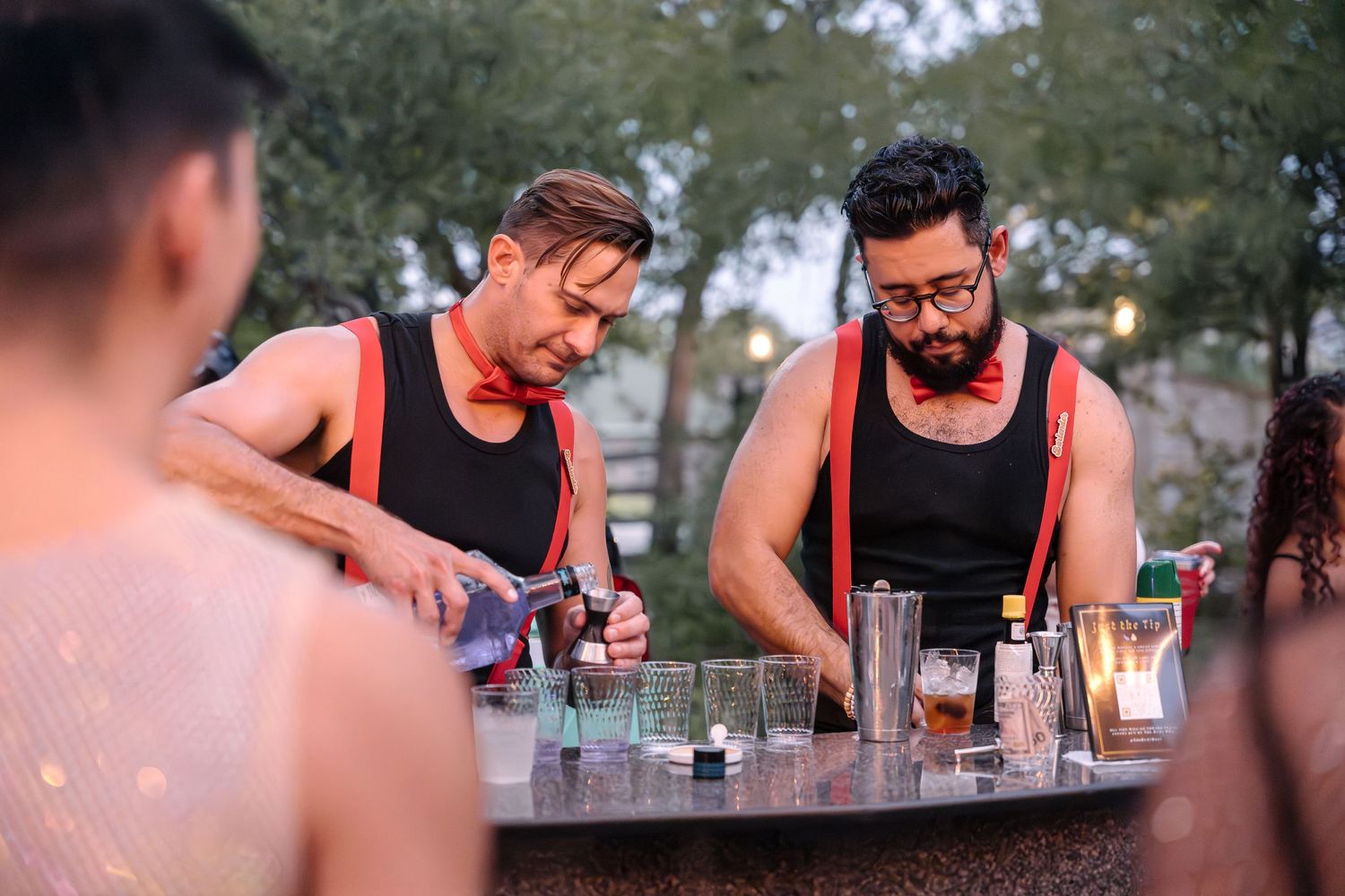 Two bartenders preparing drinks at an outdoor bar setting.