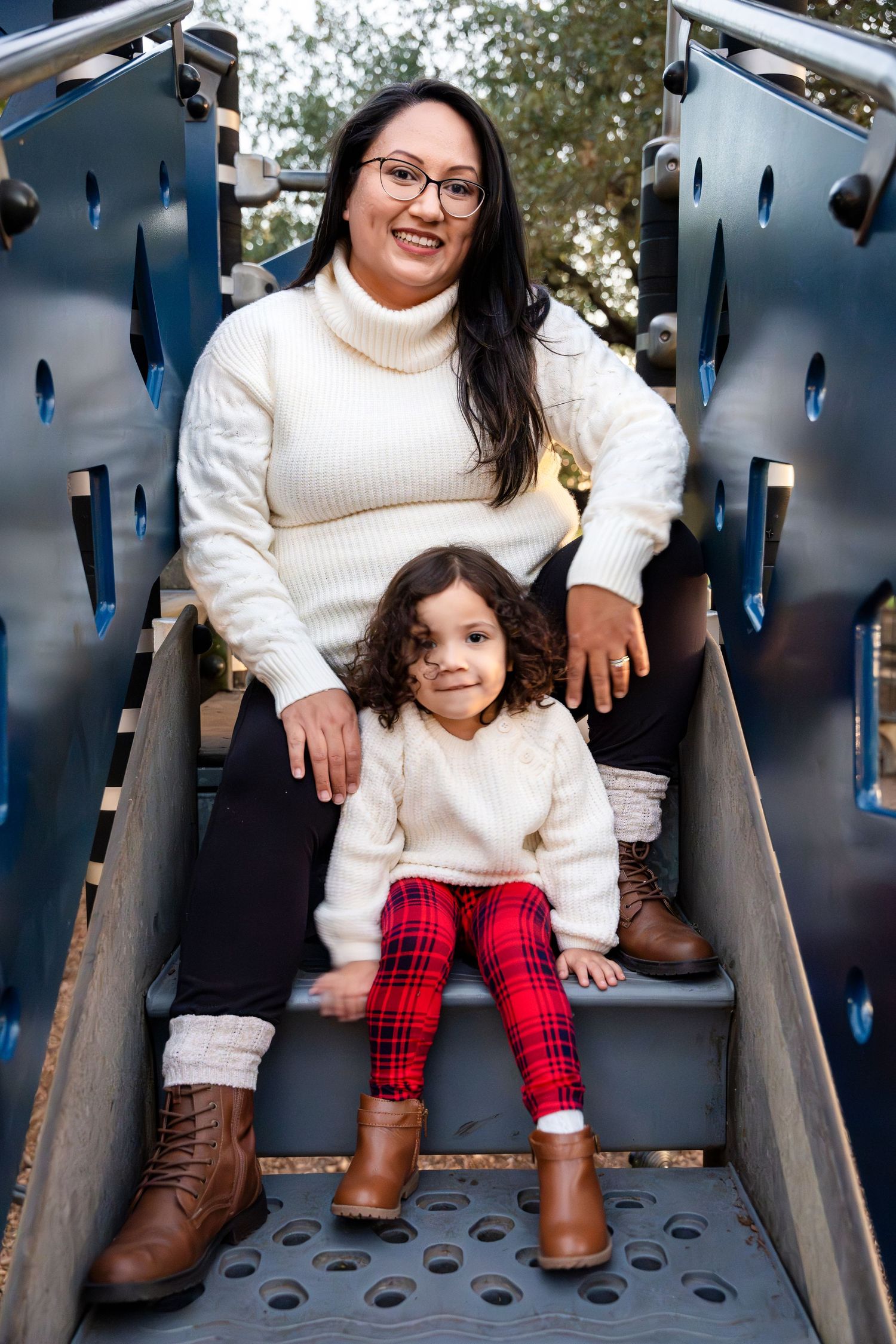 Parent and child wearing matching white sweaters pose on playground slide.