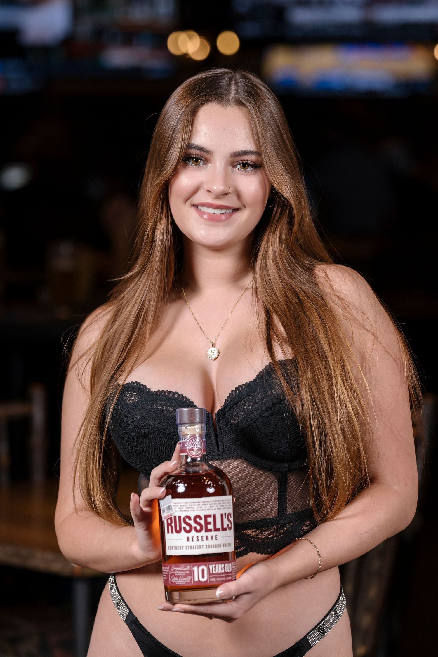 Woman in black lingerie poses with a bottle of Russell's whiskey at a bar.