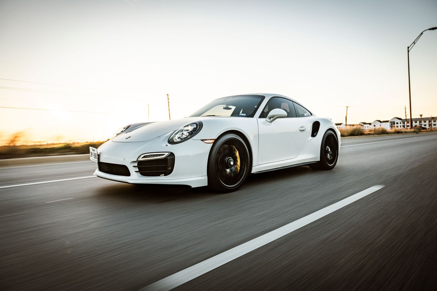 White Porsche 911 Turbo S photographed during golden hour on empty highway.