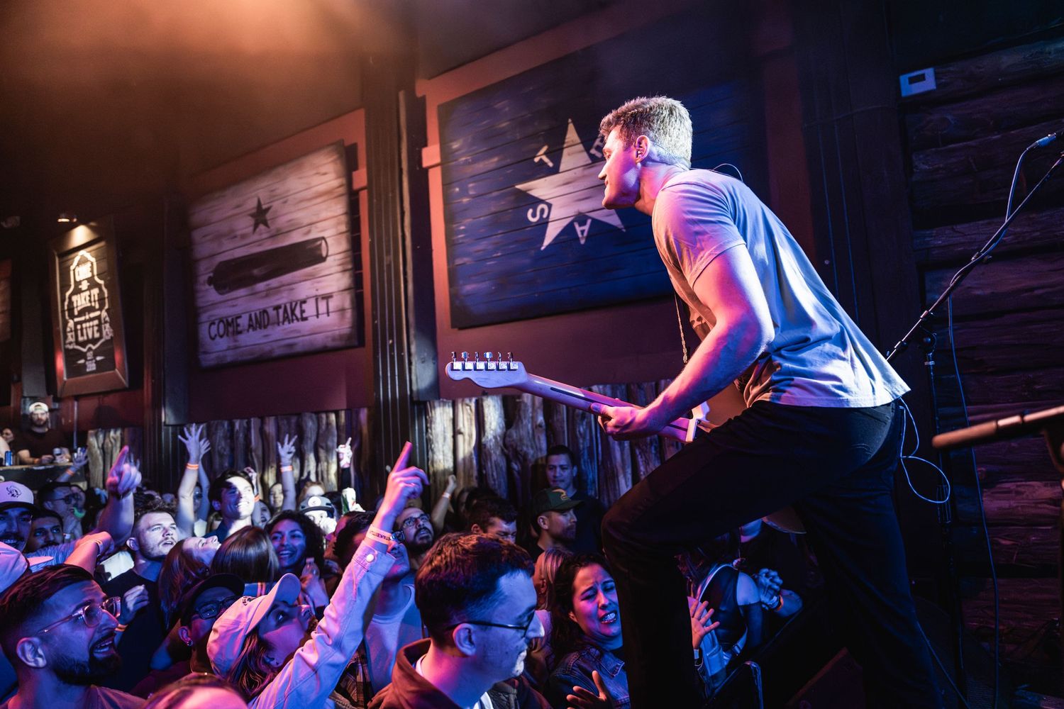 Energetic performer on stage engaging with an enthusiastic crowd at a rock concert venue.