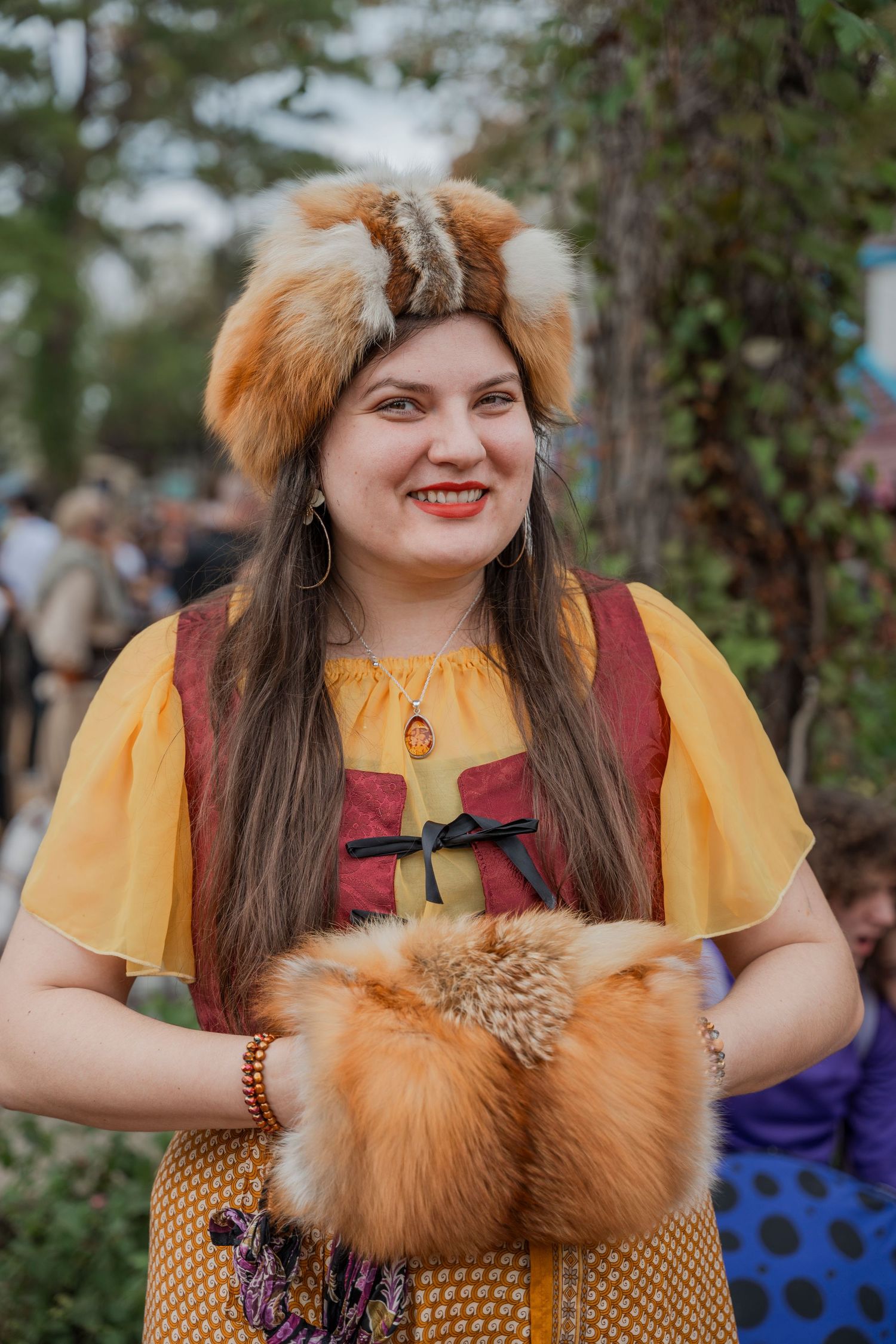 Renaissance faire attendee in yellow dress with fur accessories at outdoor festival.