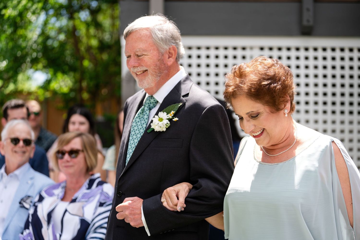 Formal couple walking arm in arm at outdoor wedding ceremony.