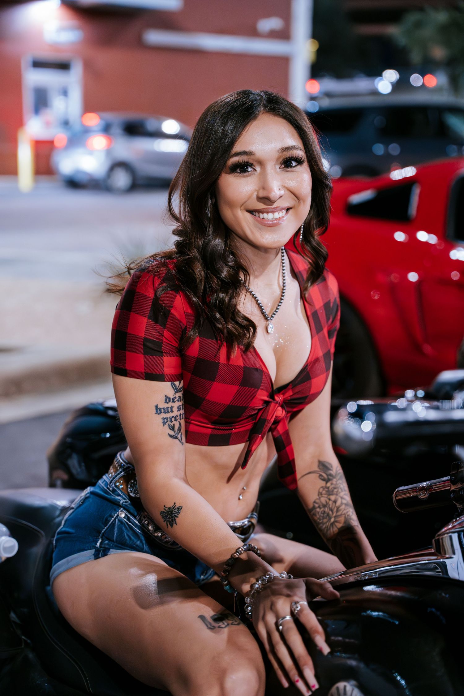 Person in buffalo plaid top posing with custom motorcycle at night.