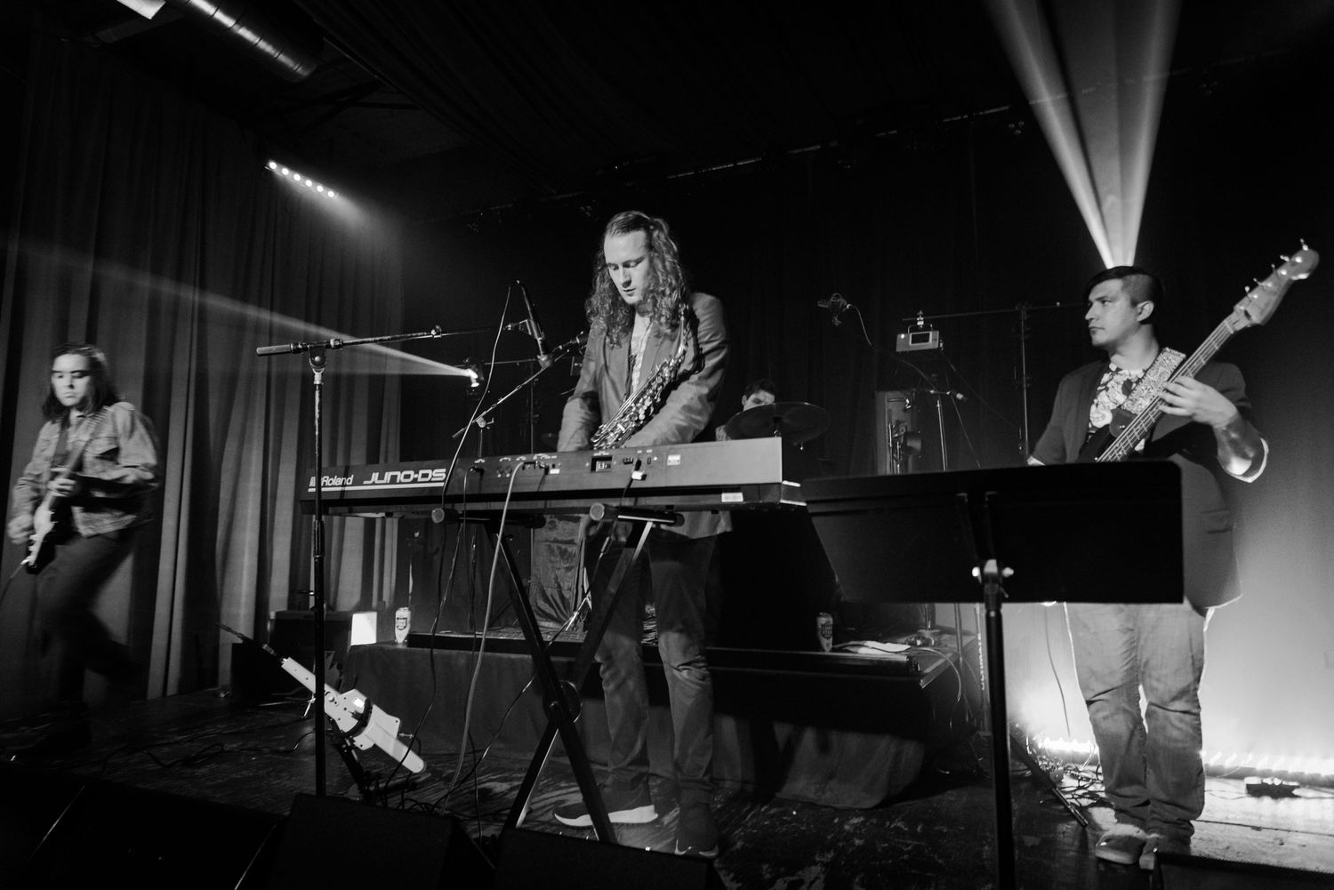 Musicians perform on stage with keyboard and instruments under venue lighting.