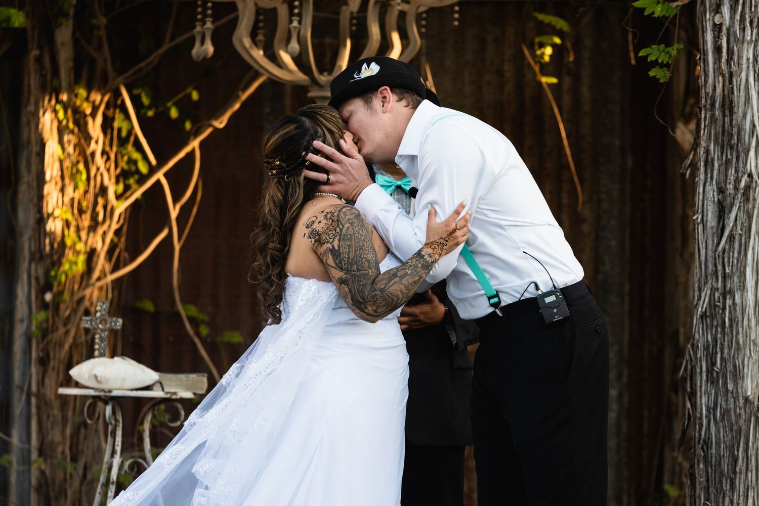 A couple shares their first kiss under a rustic wooden arch during their wedding ceremony.