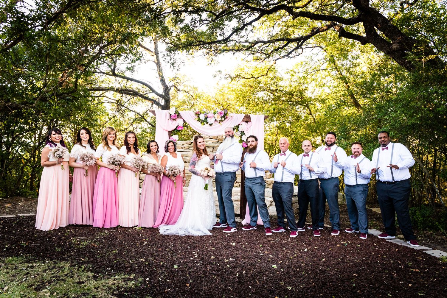 Wedding party in pink dresses and blue attire posing together on outdoor path.