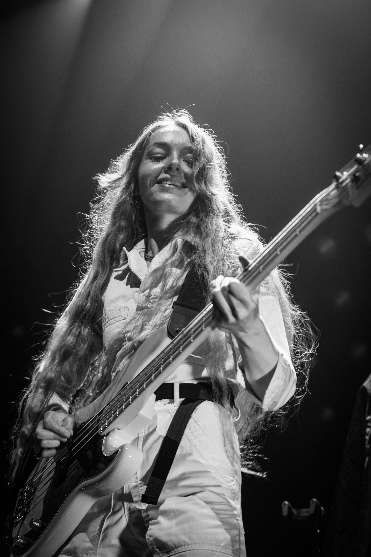 Black and white photo of bassist smiling while performing on stage.