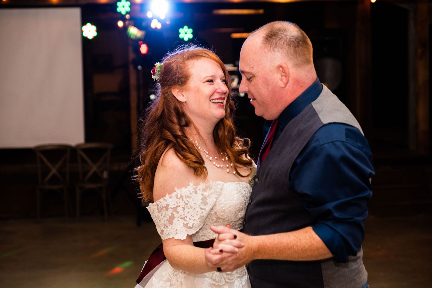 A couple shares an intimate dance moment under colorful disco lights at their wedding reception.