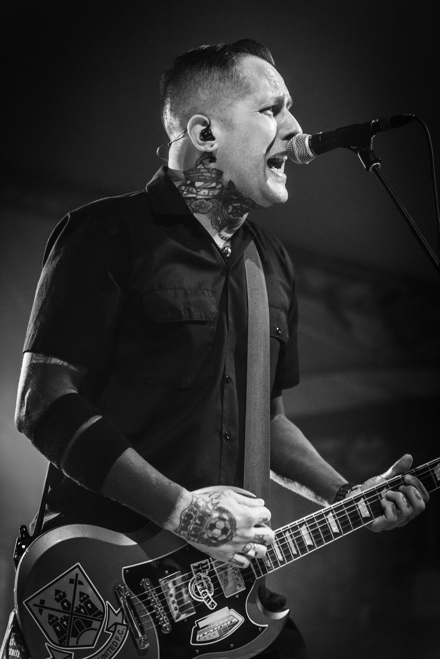 Rock musician sings passionately while playing guitar in dramatic black and white stage photo.