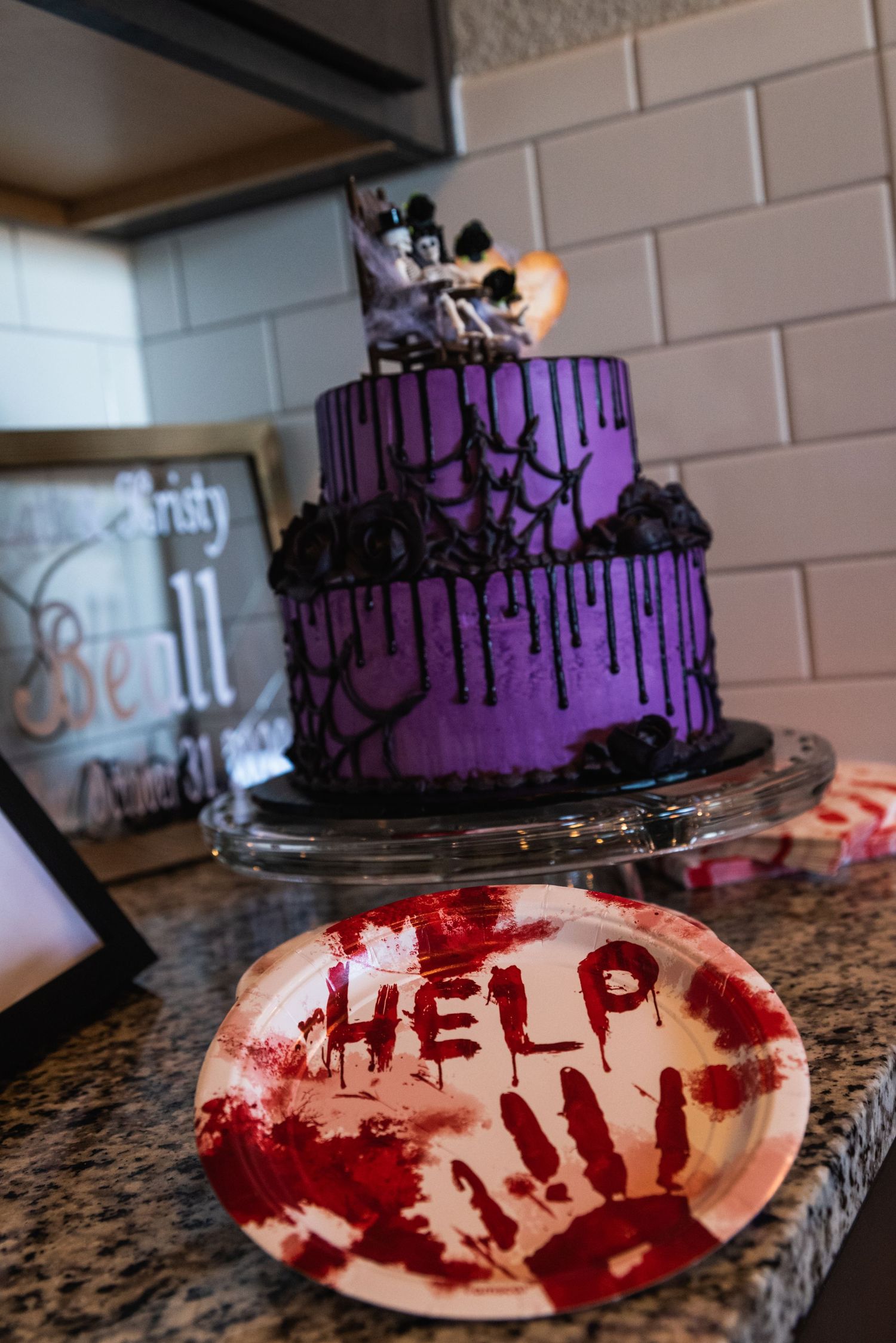 A purple Gothic wedding cake with black drips next to a bloody handprint plate reading 'HELP'.