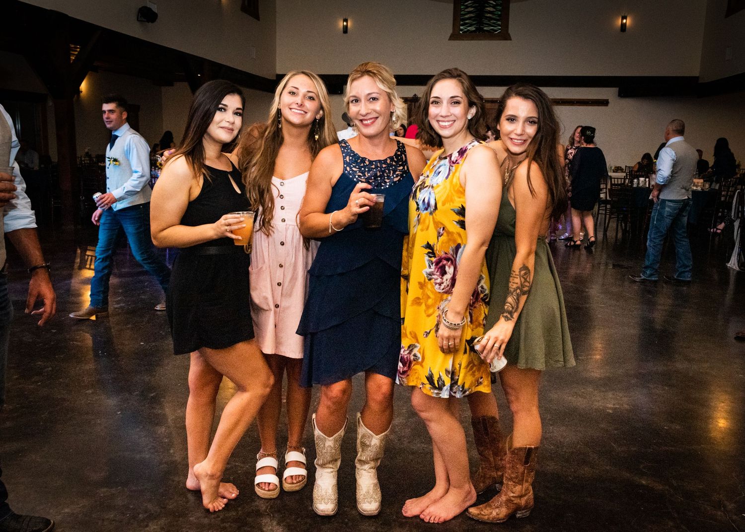 Group of wedding guests pose together at reception venue in colorful attire.
