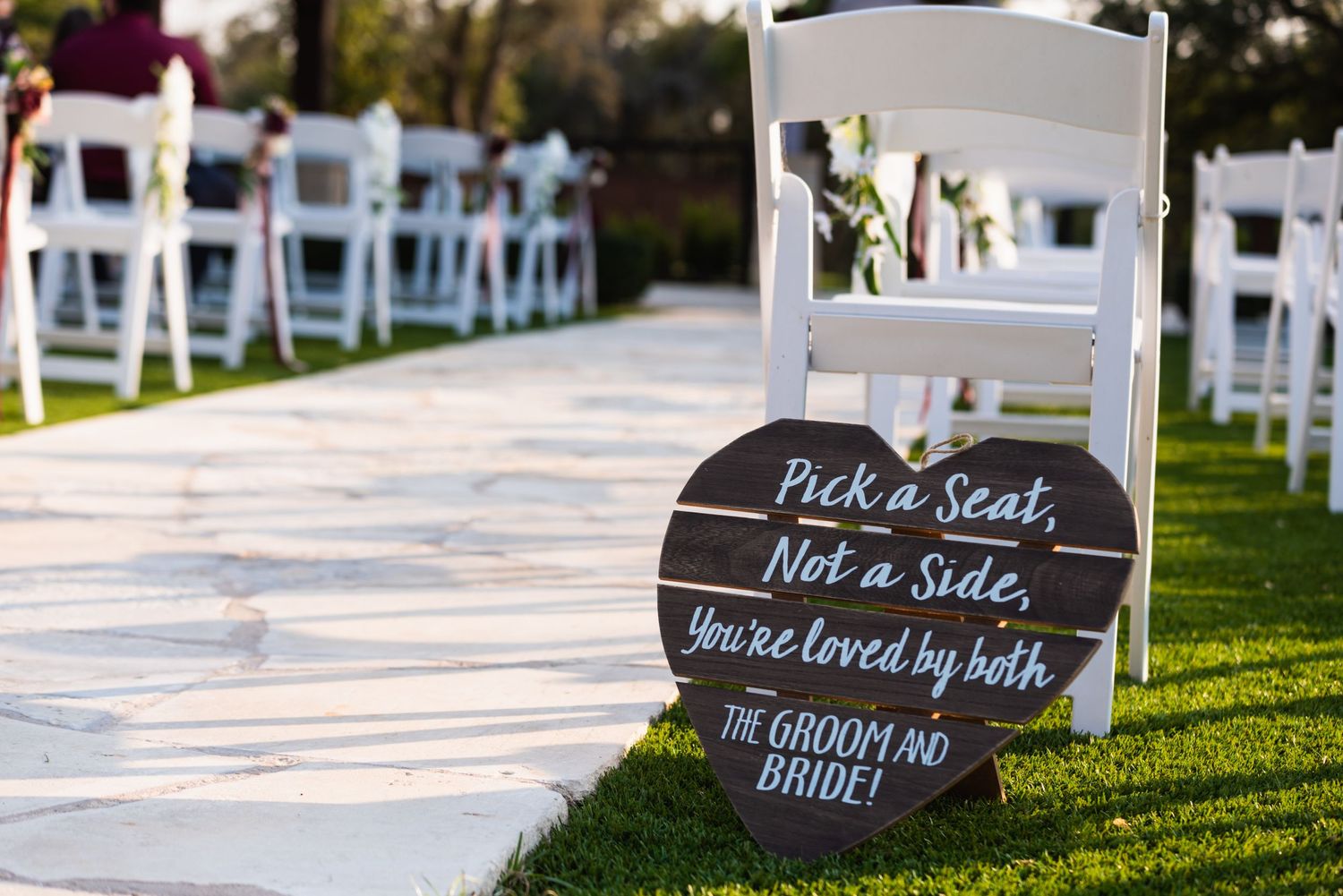 Wedding ceremony chairs set up outdoors with a sign reading Pick a seat, not a side.