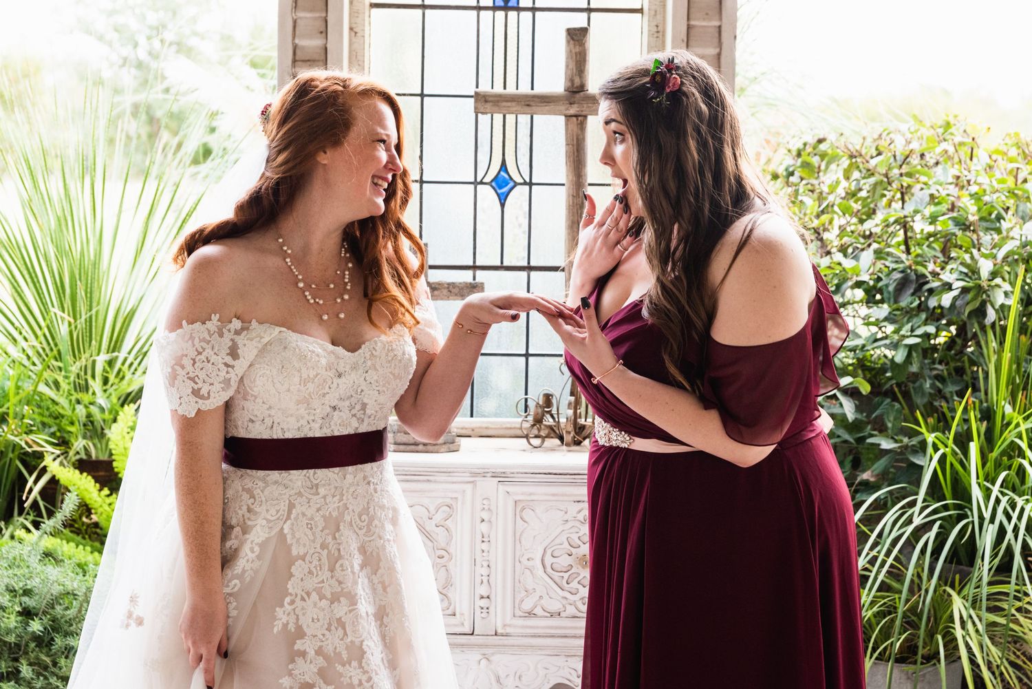 Bride and bridesmaid share a joyful moment in an elegant chapel setting.