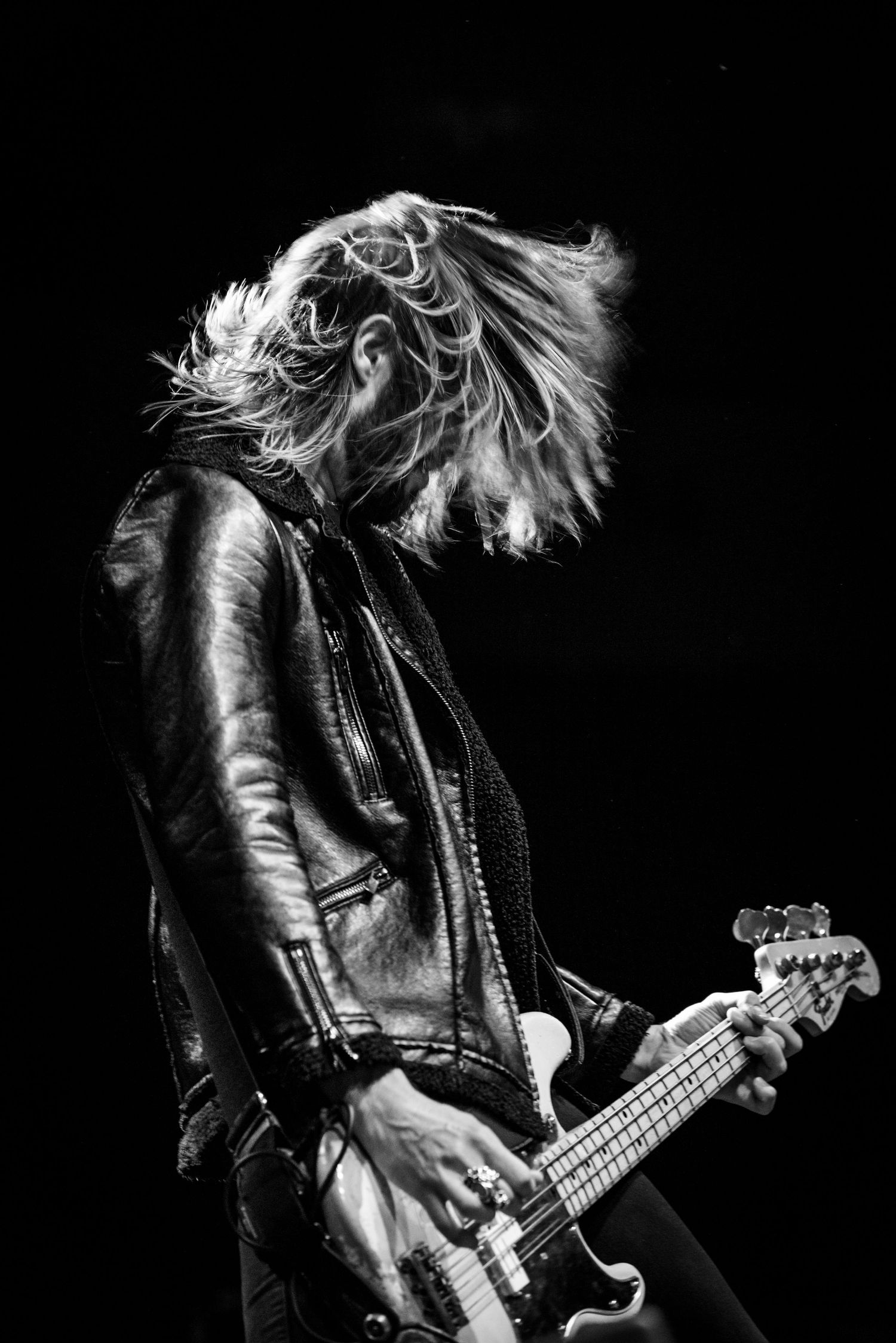 Dramatic black and white shot of bassist with hair in motion during performance.