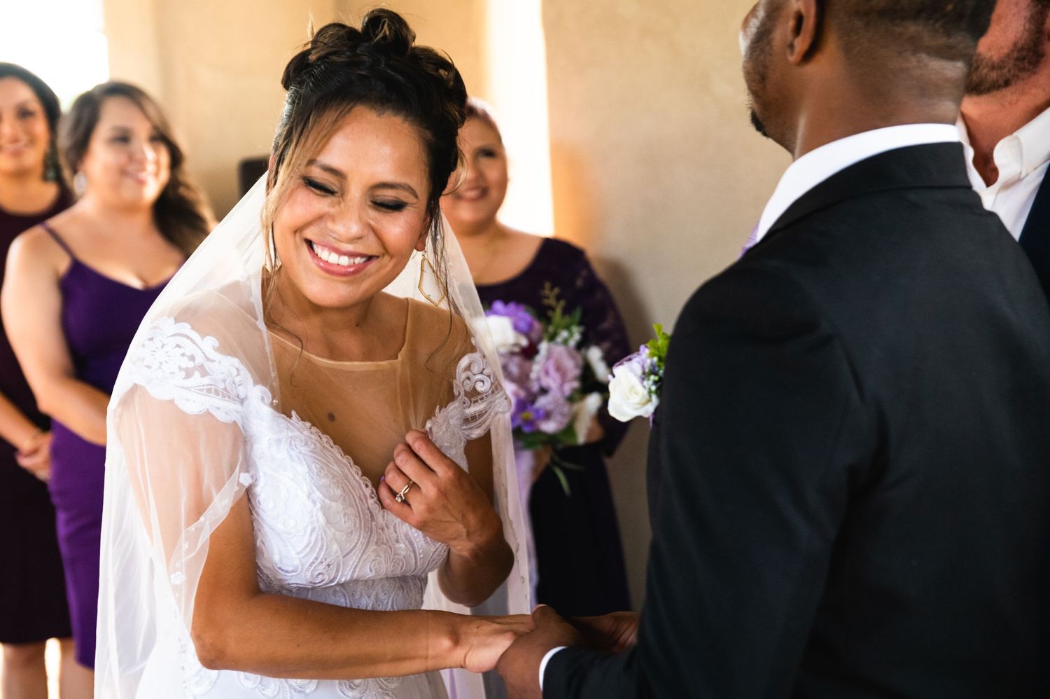 Wedding ceremony indoors with couple exchanging vows and holding purple floral bouquet.