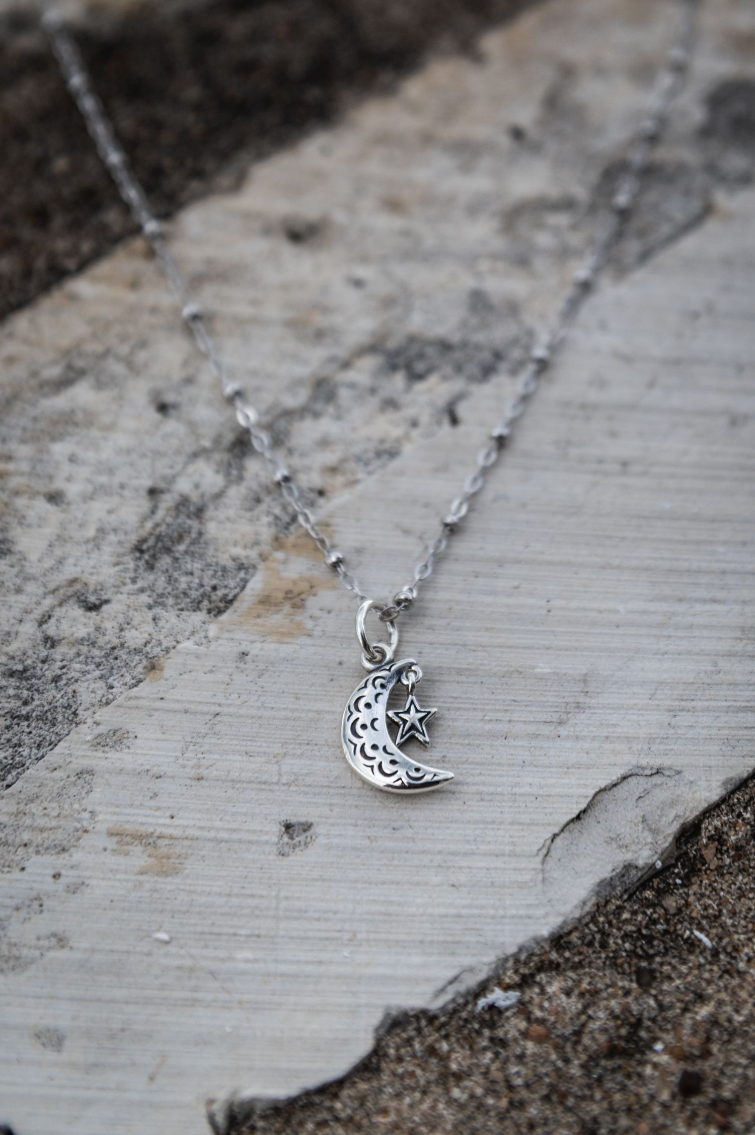 Delicate silver crescent moon pendant necklace on a weathered white wooden surface.