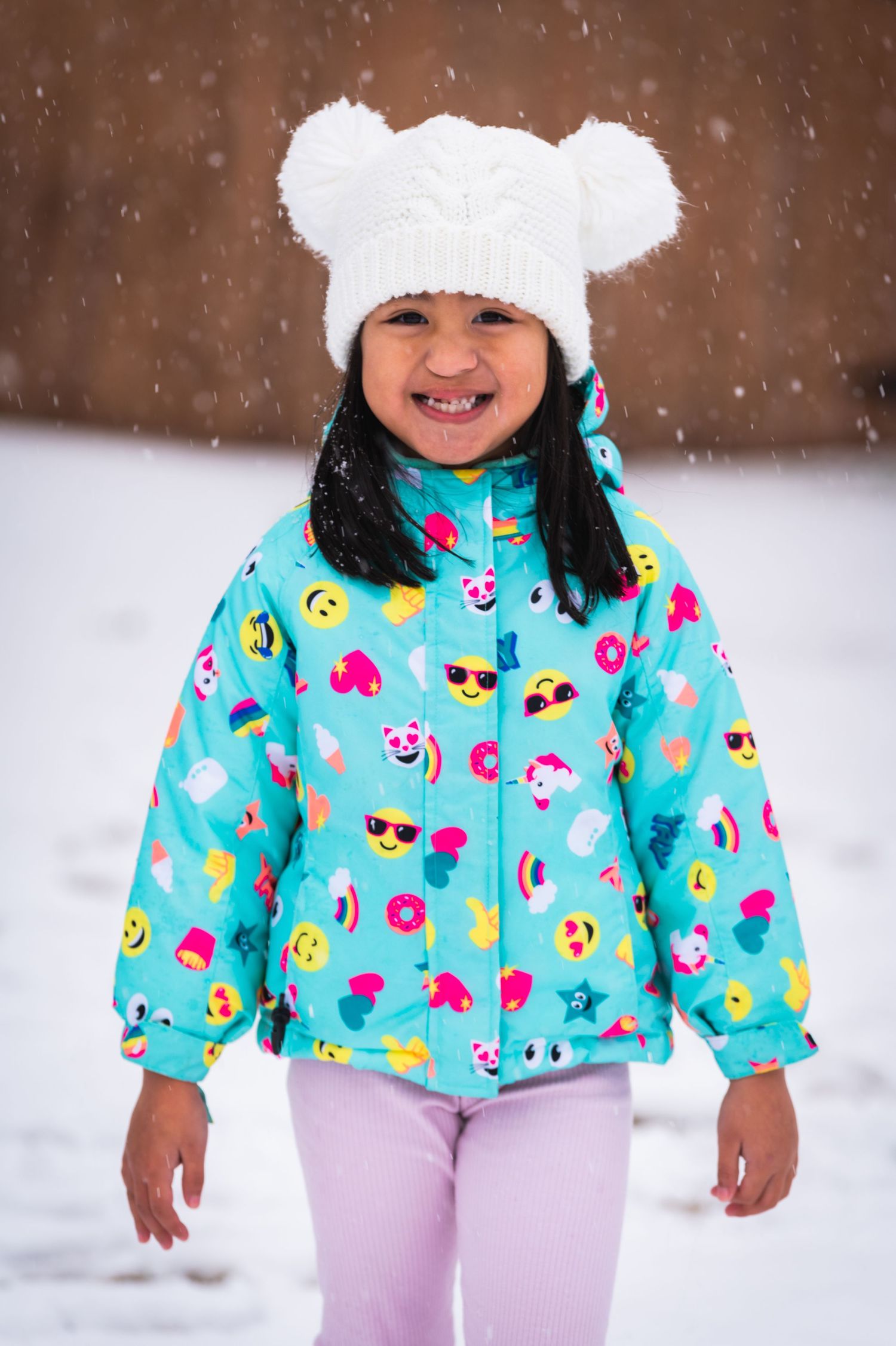 A child in a bright blue patterned coat and white bear hat stands in the snow.