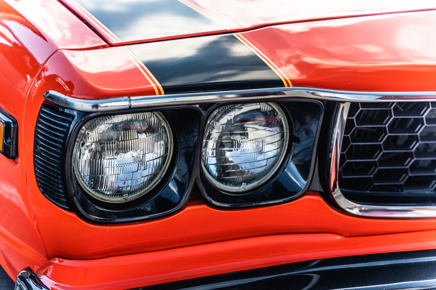 Close-up of dual headlights on an orange classic muscle car with black grille detail.