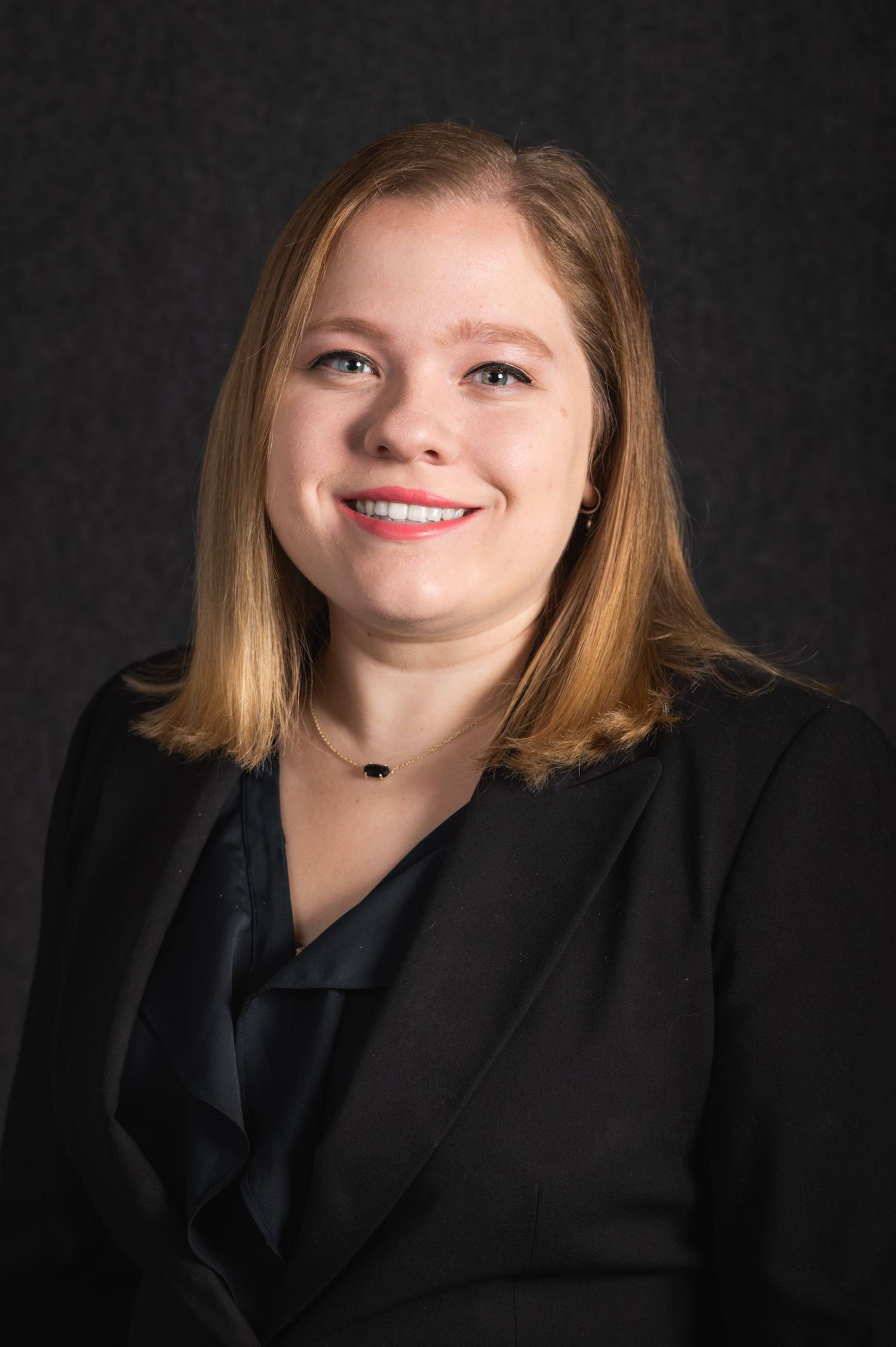 Professional headshot against dark background wearing black business attire.
