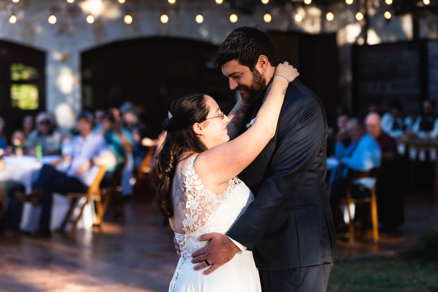 A romantic dance moment between newlyweds under twinkling lights at their evening reception.