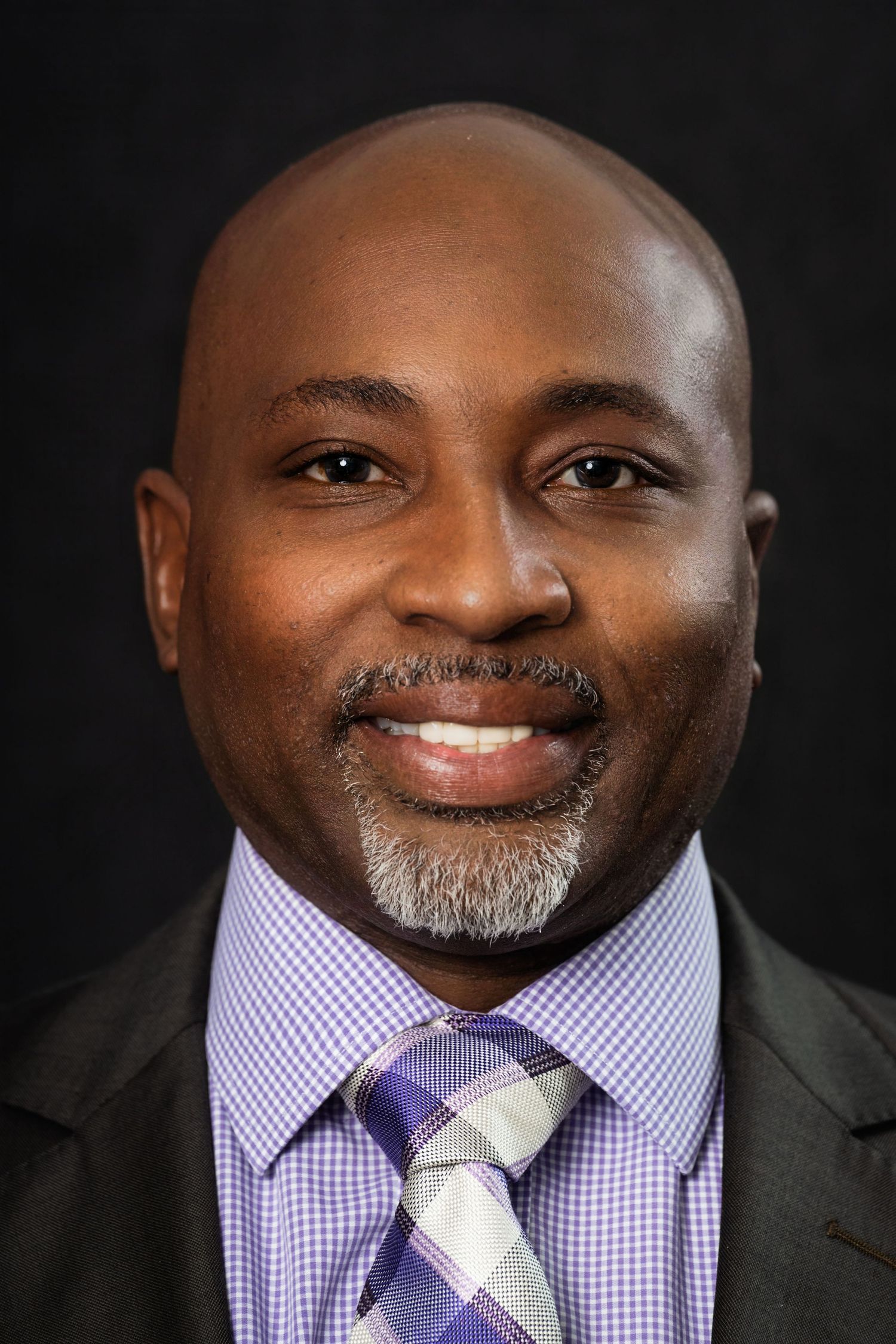 Professional headshot of a person wearing a purple patterned tie and dark suit.