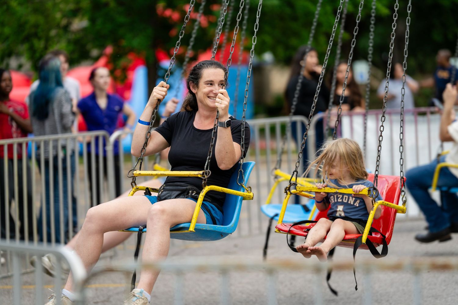 Woman and child enjoying a chain swing ride at an outdoor amusement park on a summer day.