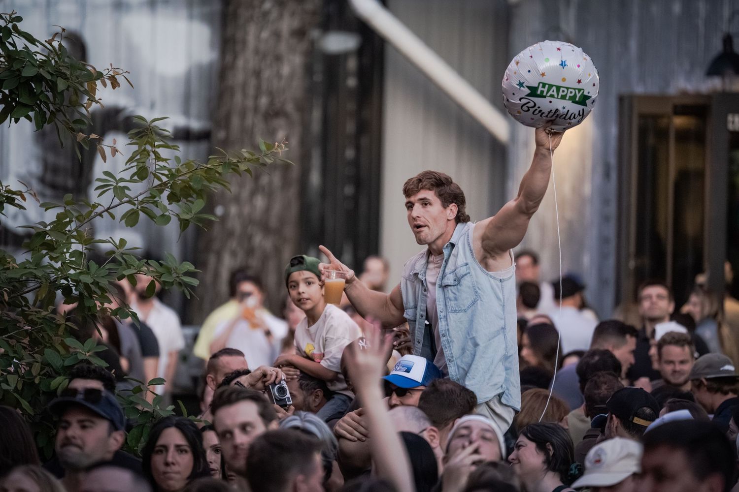A man raises a soccer ball above a large outdoor crowd at a lively event.