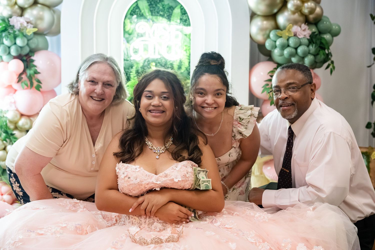 Family posing together at a quinceañera celebration with balloon arch backdrop and pink ruffled dress.