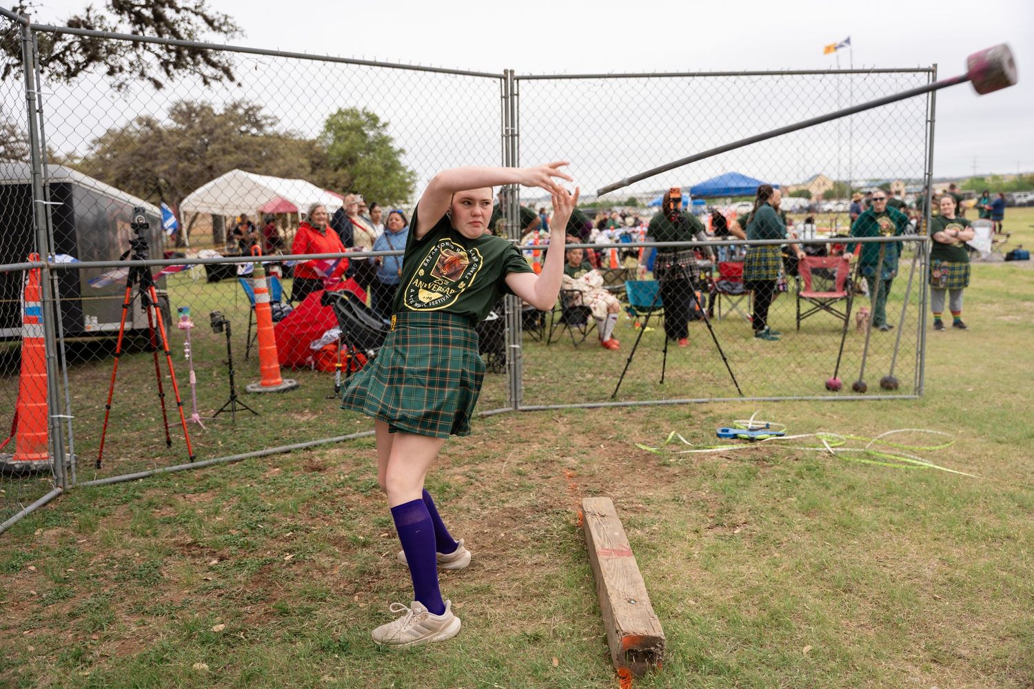 Woman in tartan kilt throwing hammer at Highland Games competition outdoors.