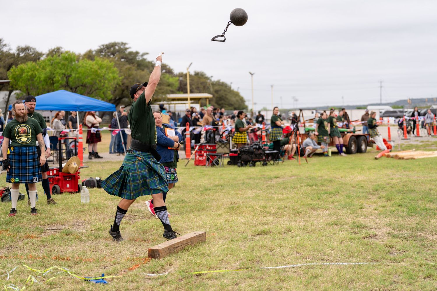 Athlete in tartan kilt throws weight over bar at Scottish Highland Games competition outdoors.