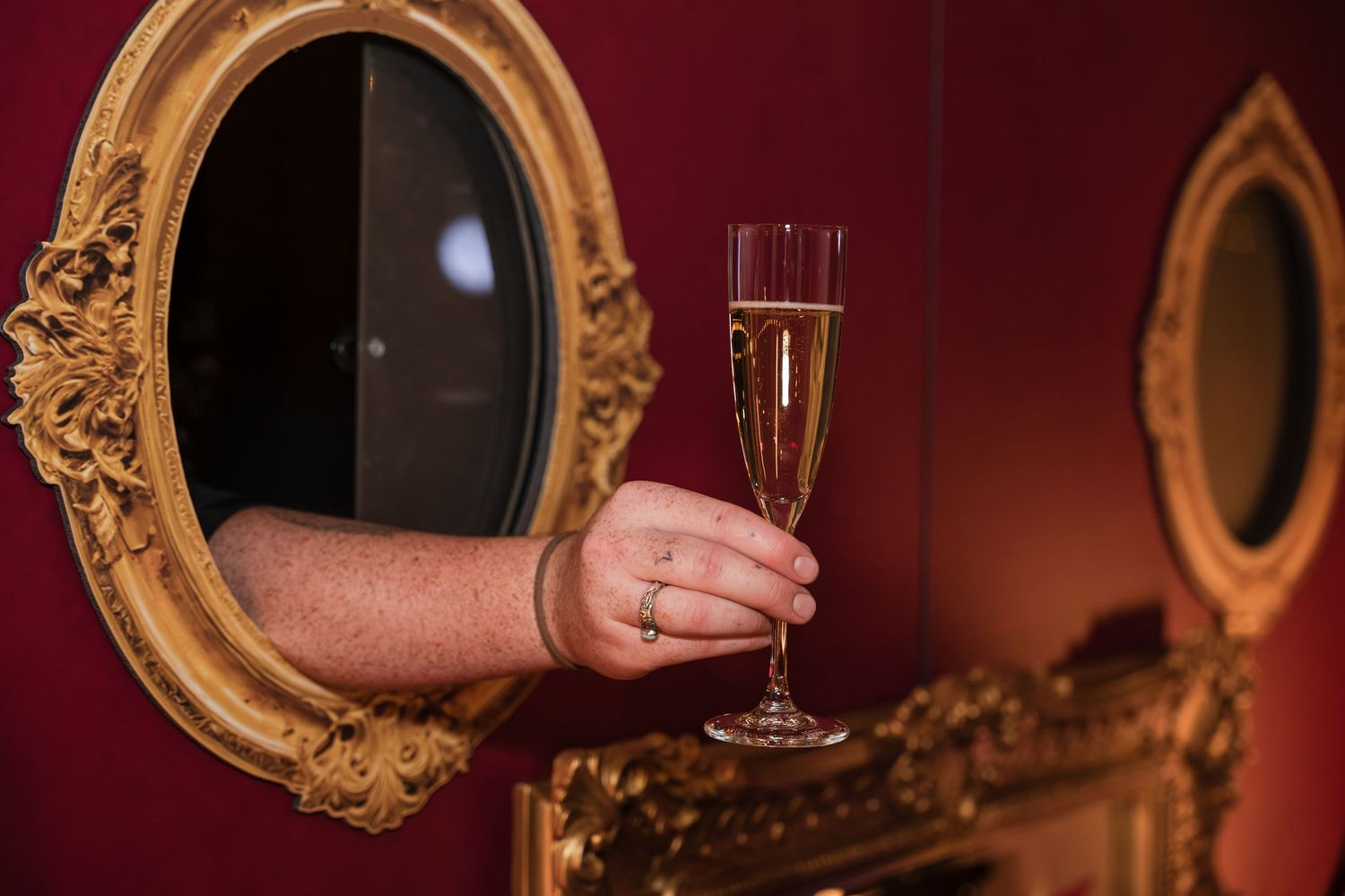 A person holding a glass of champagne in front of an ornate gold mirror in a dimly lit room.