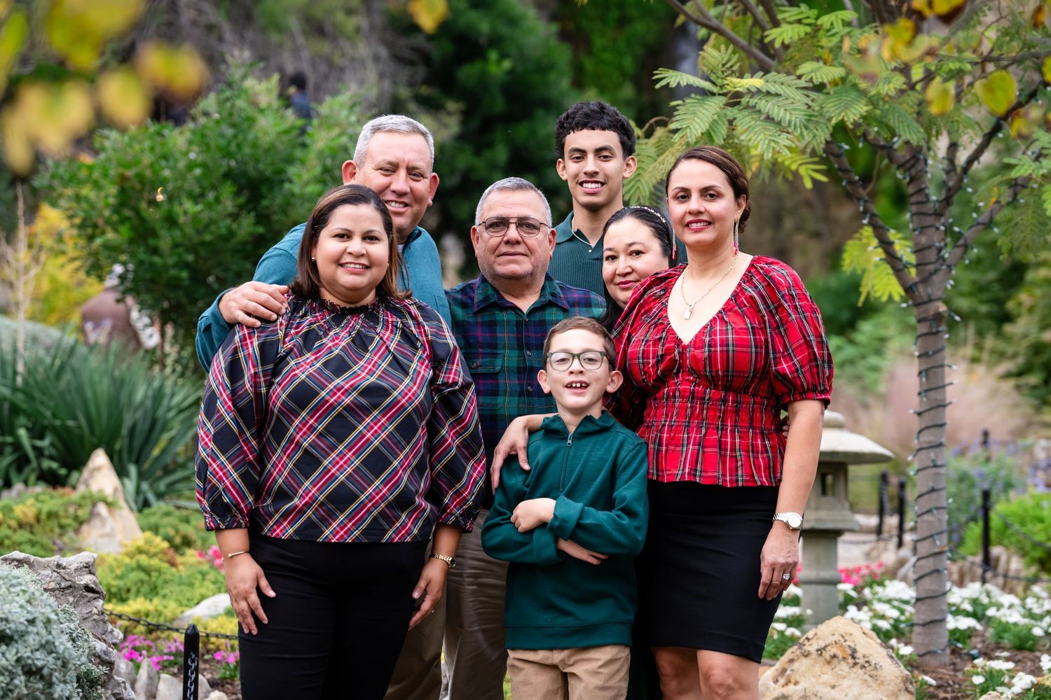 A family wearing coordinated red and black plaid shirts poses together outdoors during autumn.