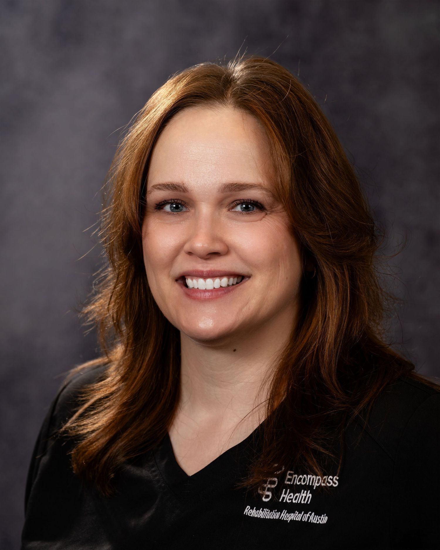 Professional headshot portrait of person with red hair and warm smile against dark background.