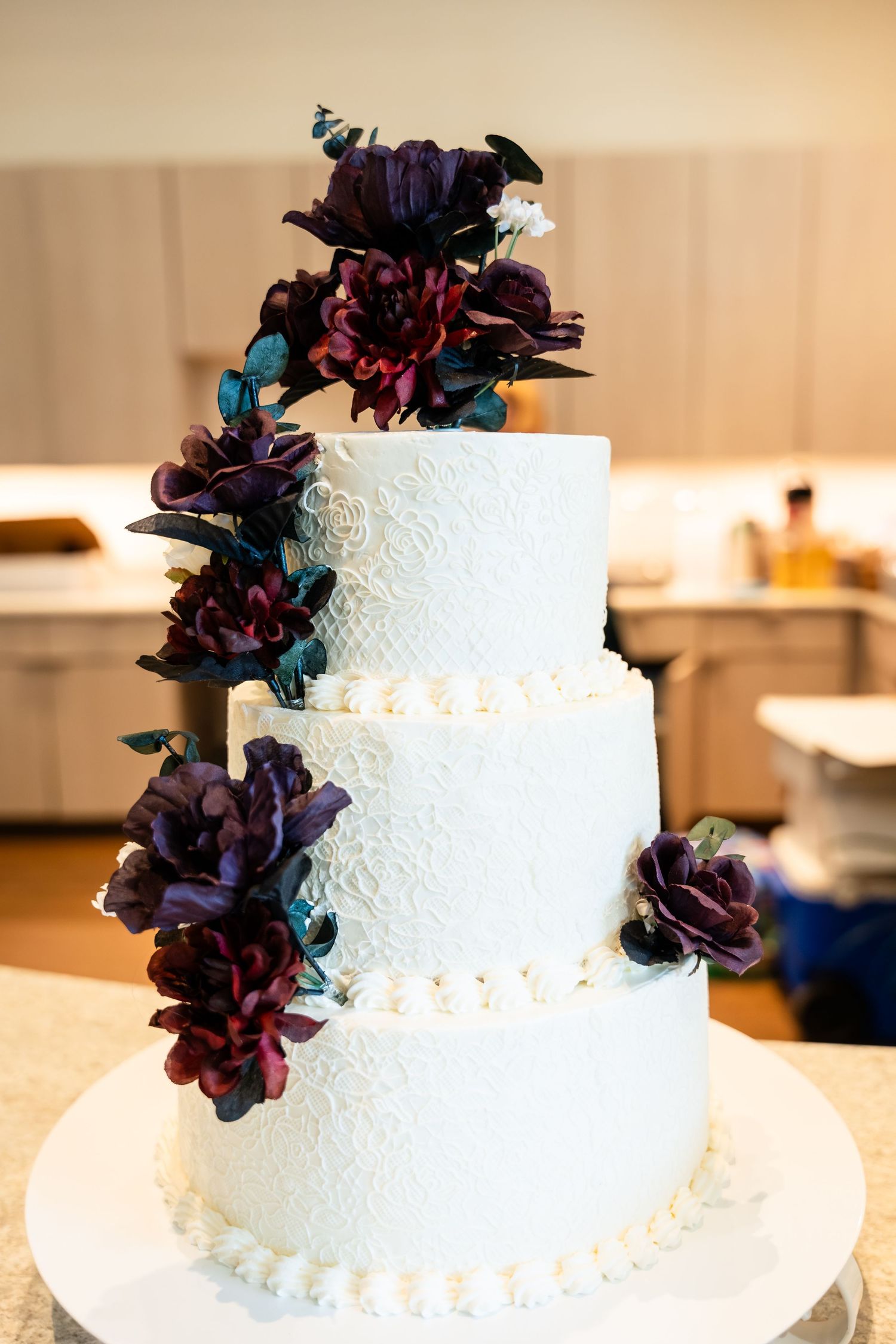 White wedding cake decorated with delicate lace patterns and deep purple floral accents on display.