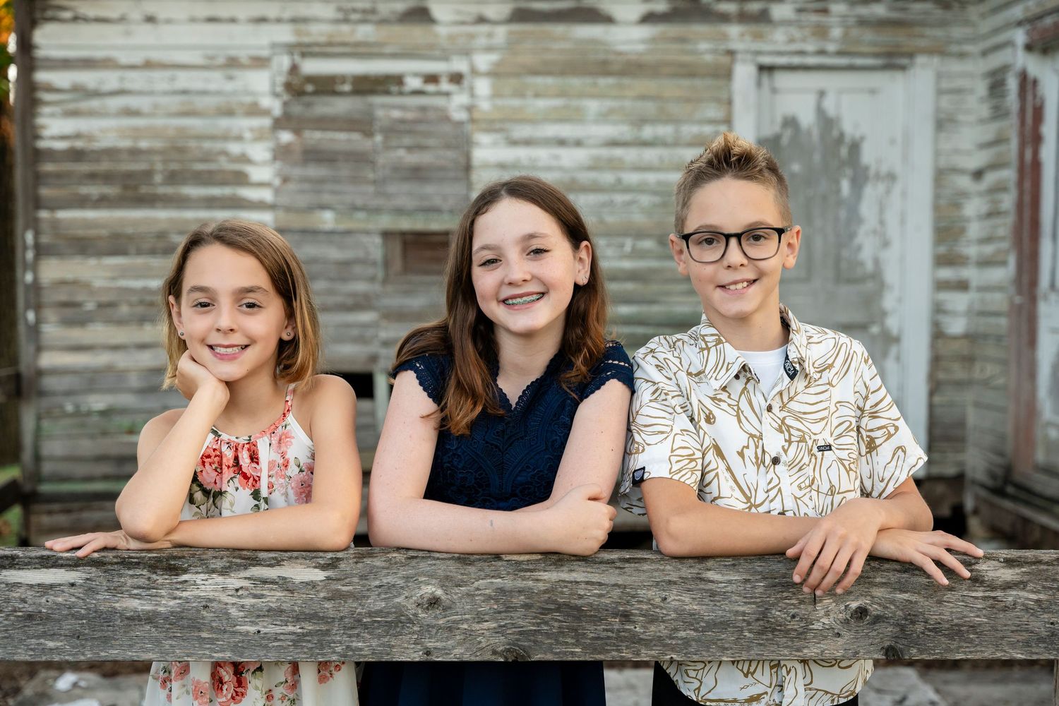 A group of people lean against a rustic wooden wall while posing together for a casual outdoor portrait.