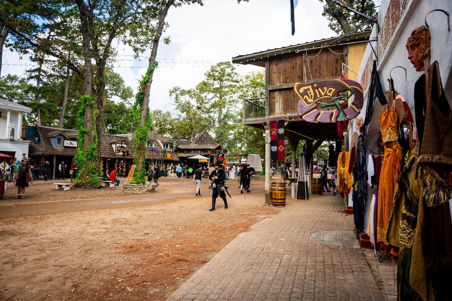 Colorful market stalls and shops line a rustic walkway in a tropical tourist destination with palm trees overhead.