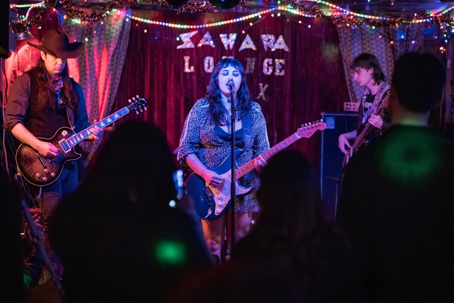 Musicians perform on stage with colorful red and blue lighting at a live music venue.