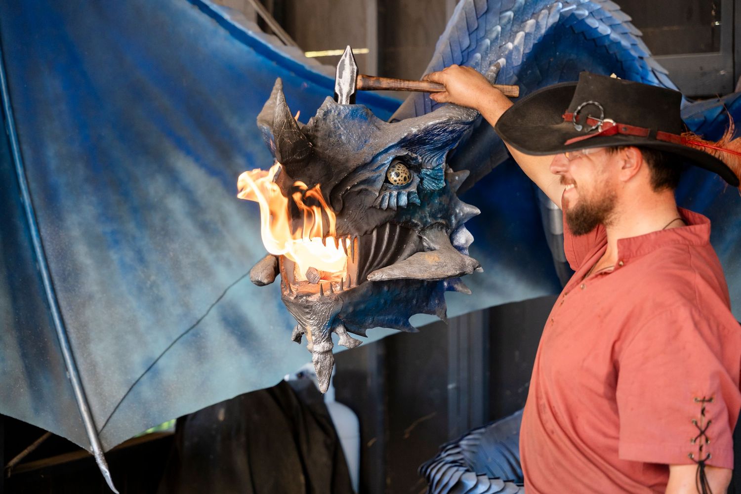 A person in a red shirt and baseball cap examines a mechanical dragon prop with glowing eyes and flames.