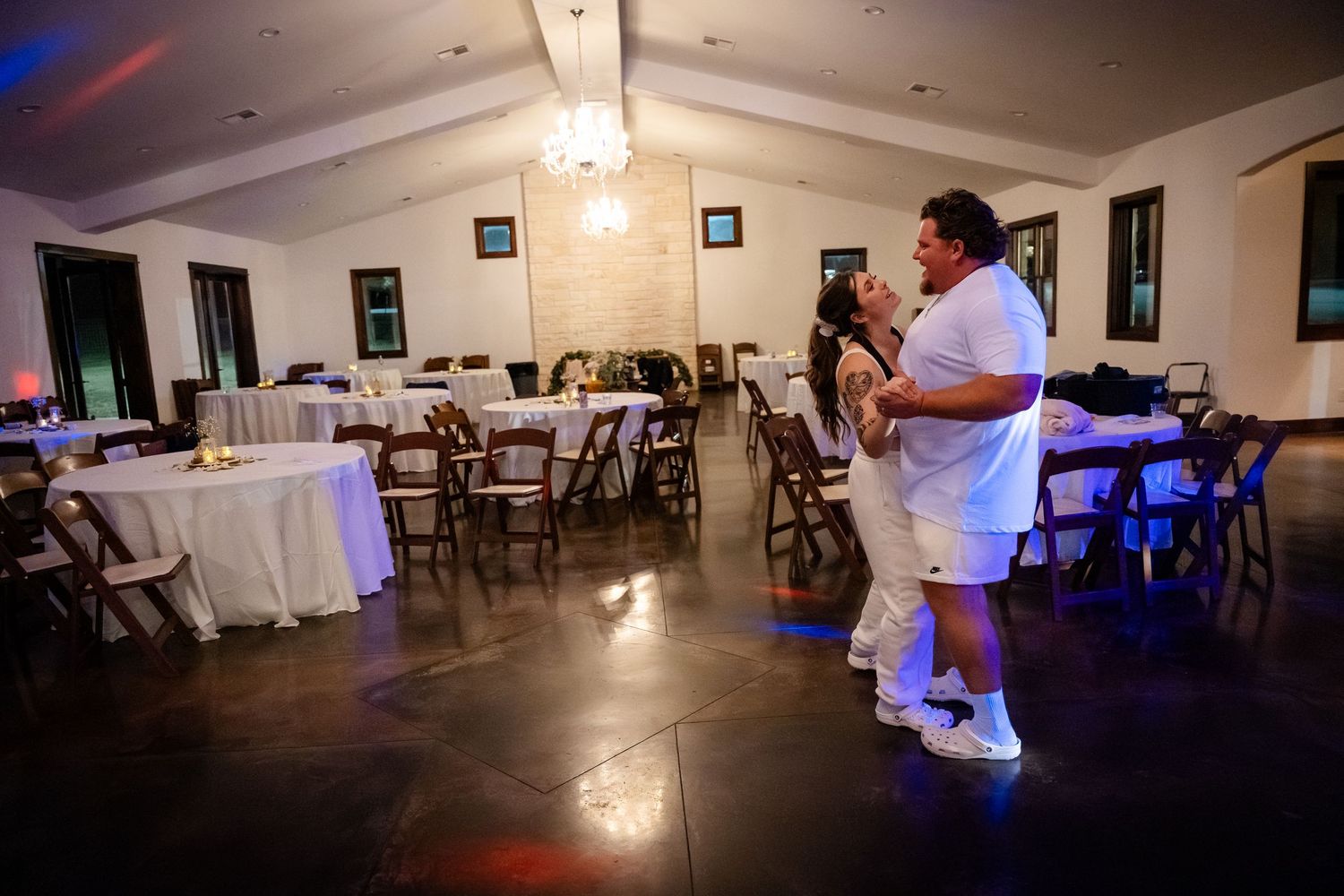 Couple shares first dance in elegant wedding reception hall with white tablecloths and warm lighting.