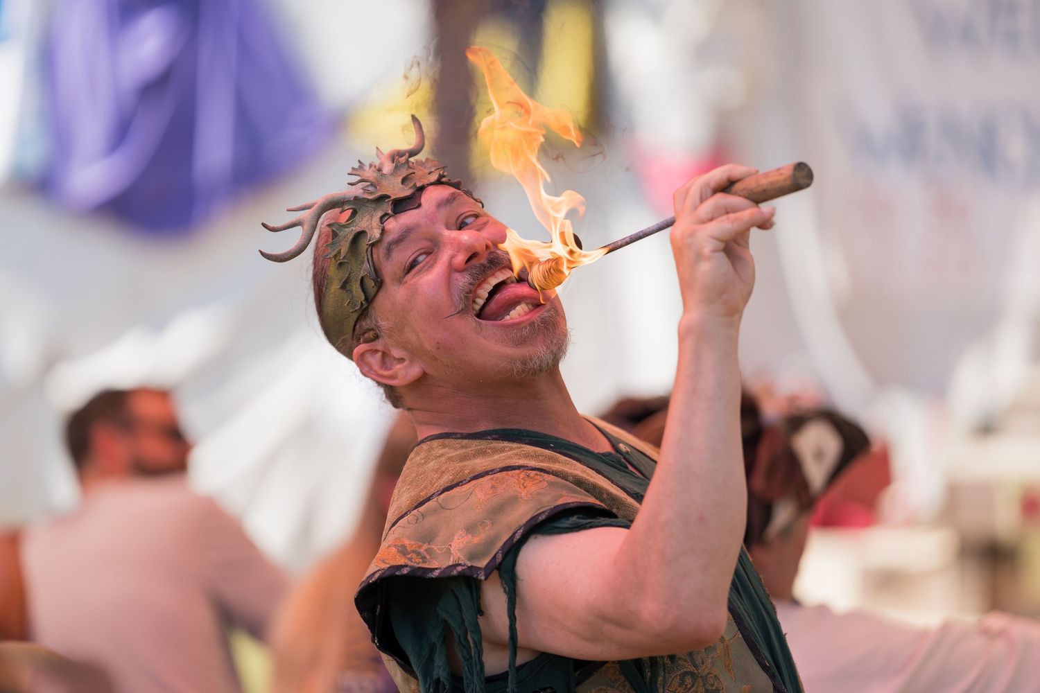 A performer in a black tank top breathes fire during an outdoor festival performance.
