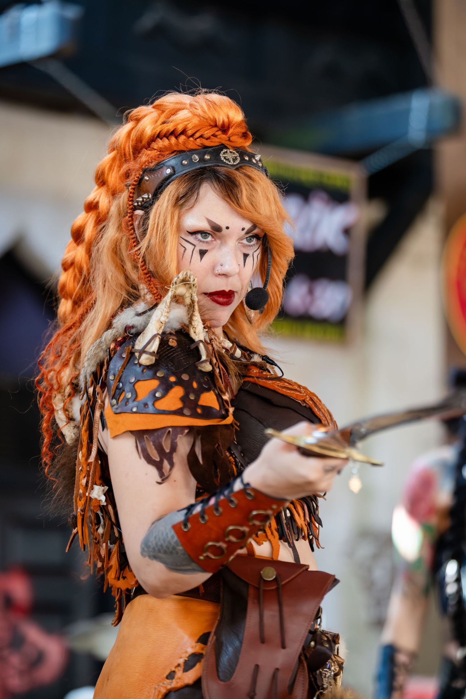 Steampunk performer in orange and brown costume with decorative face paint performs at a festival.