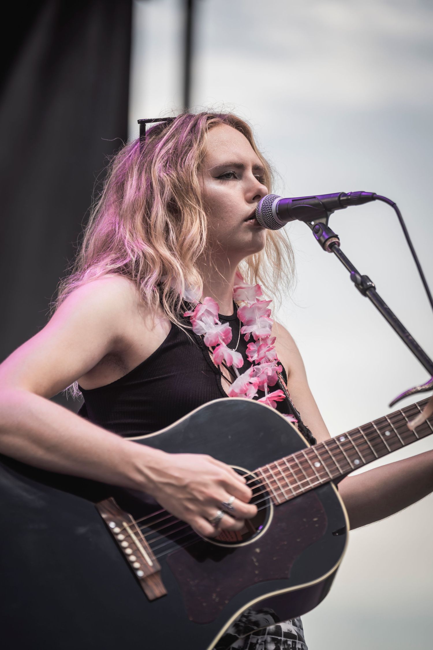 A musician performs on stage with an acoustic guitar while singing into a microphone during a live performance.