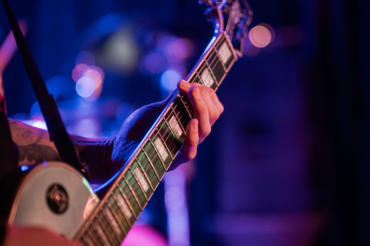Close-up shot of hands playing electric guitar with colorful stage lighting in the background.