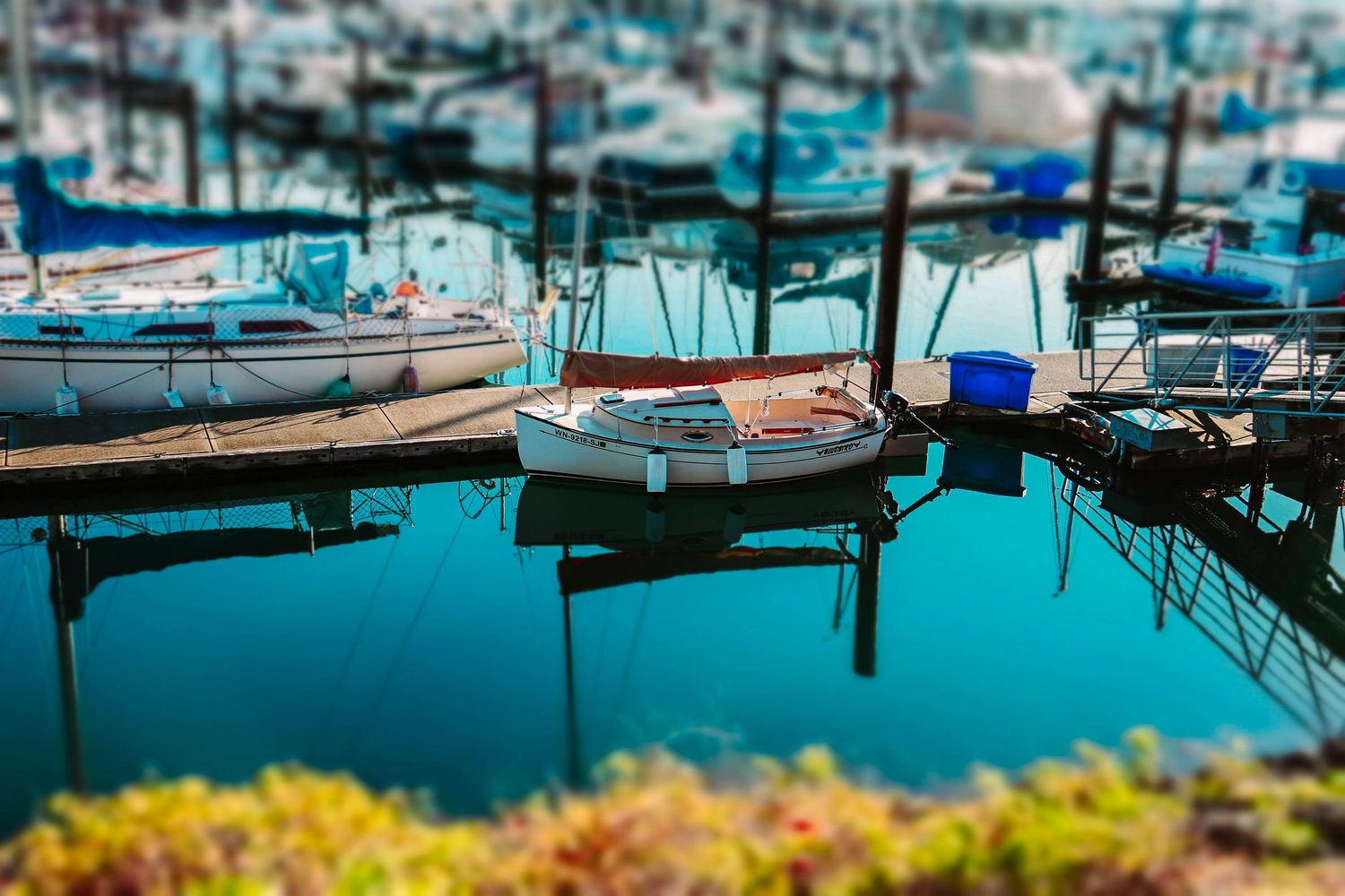 Sailboats moored in a marina with calm turquoise waters creating reflections.