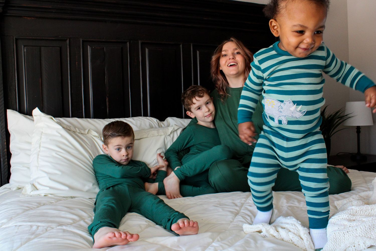 Children in matching pajamas play together on a white bed.