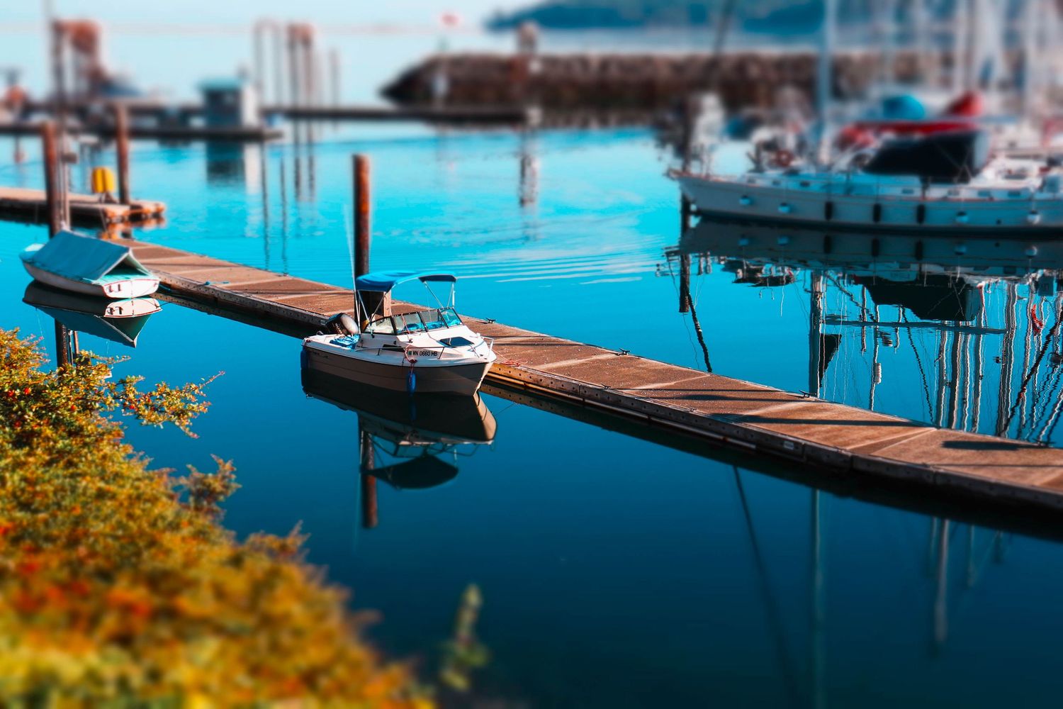 Small boats docked along wooden pier with tilt-shift effect creating miniature look.