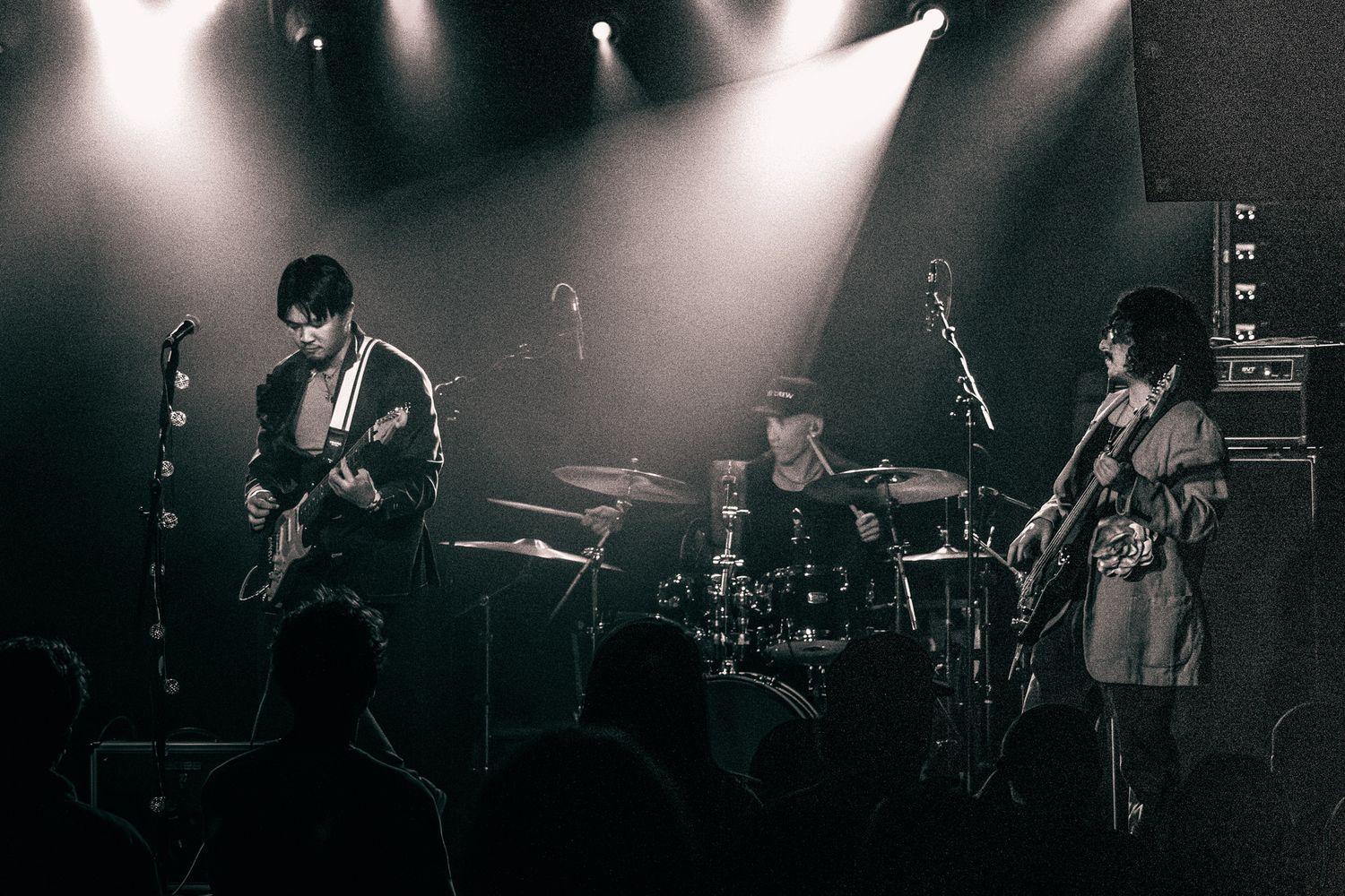 Black and white photo of a rock band performing on stage under dramatic spotlights before a live audience.
